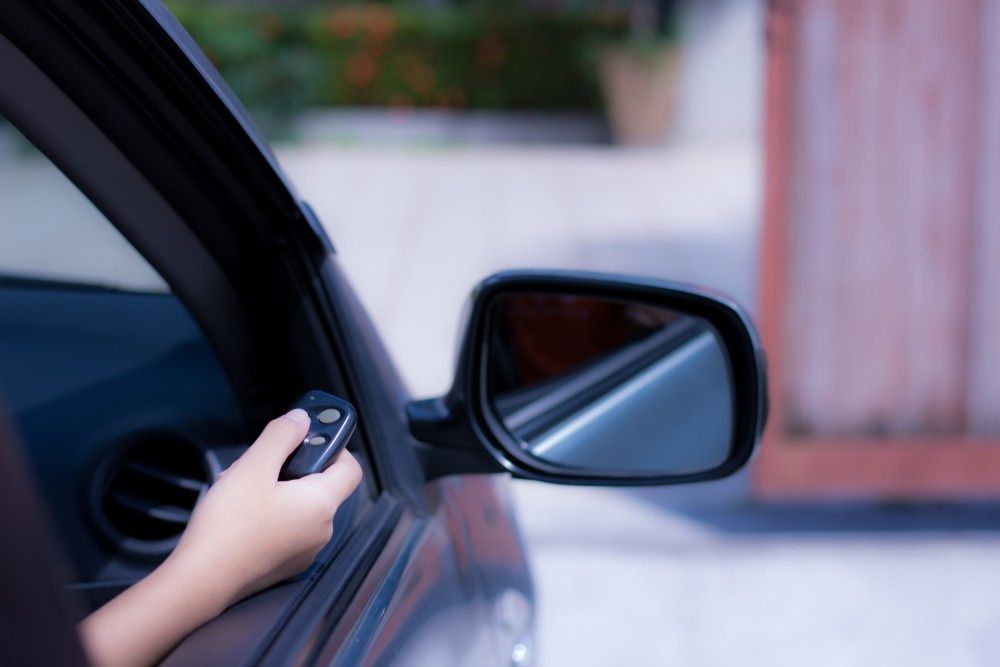 A Person Is Holding a Remote Control in Their Hand While Driving a Car — Gem Garage Doors in Bellingen, NSW