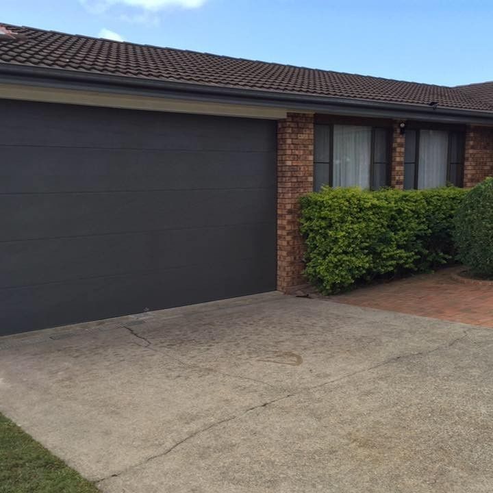 A Black Garage Door Is Sitting in Front of A Brick House — Gem Garage Doors in Coffs Harbour, NSW