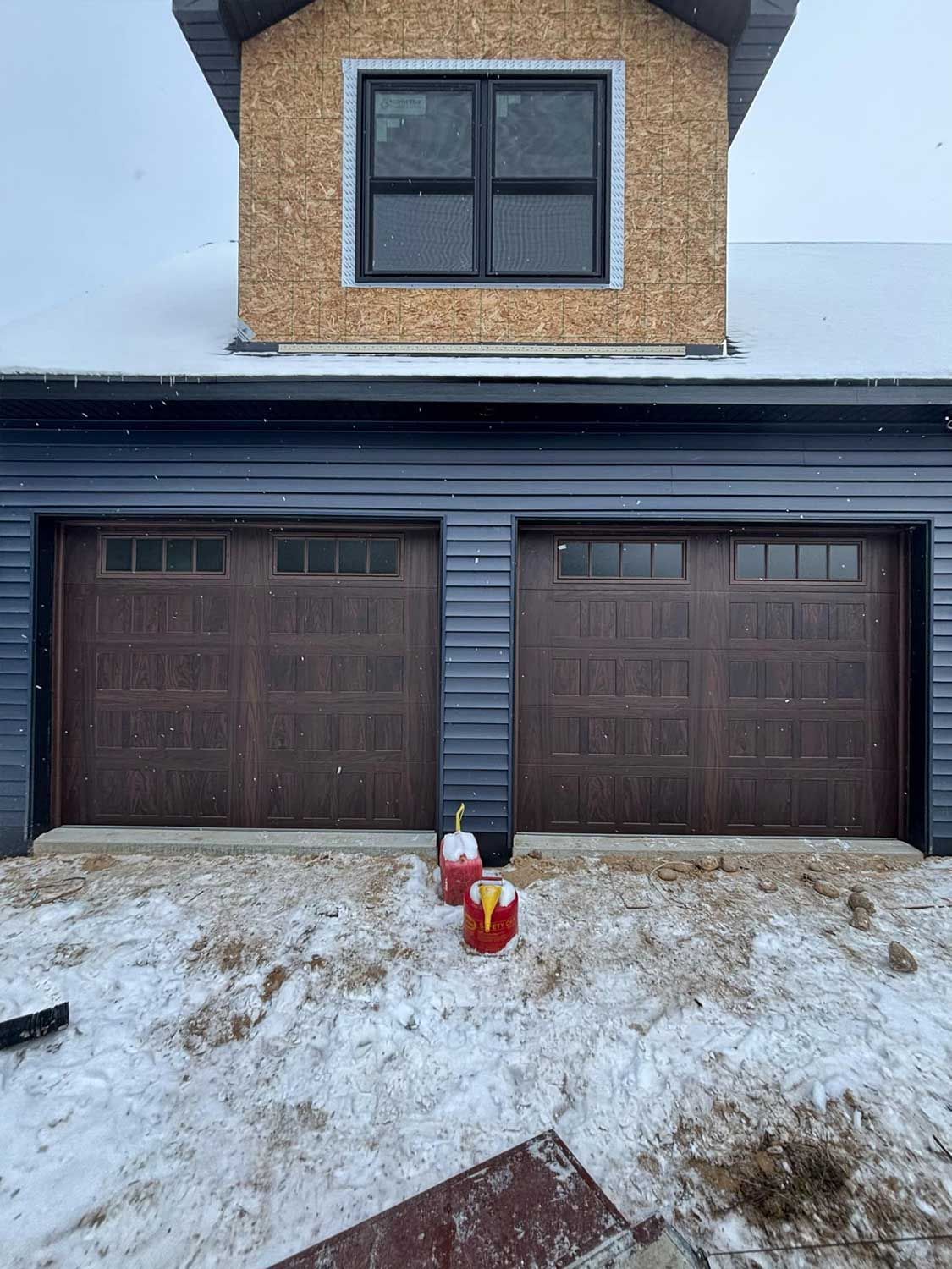 garage doors and a brick dormer window above