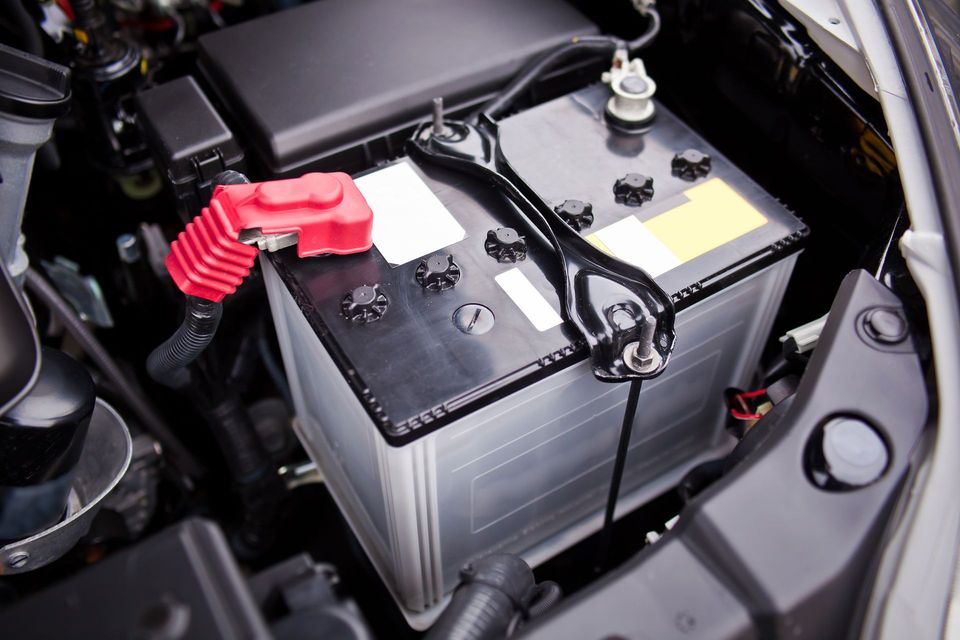 Car battery in a vehicle engine bay with red and black terminals and cables connected