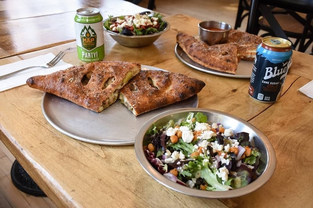Pizza slices, salads, and soda cans on a wooden table in a casual dining setting