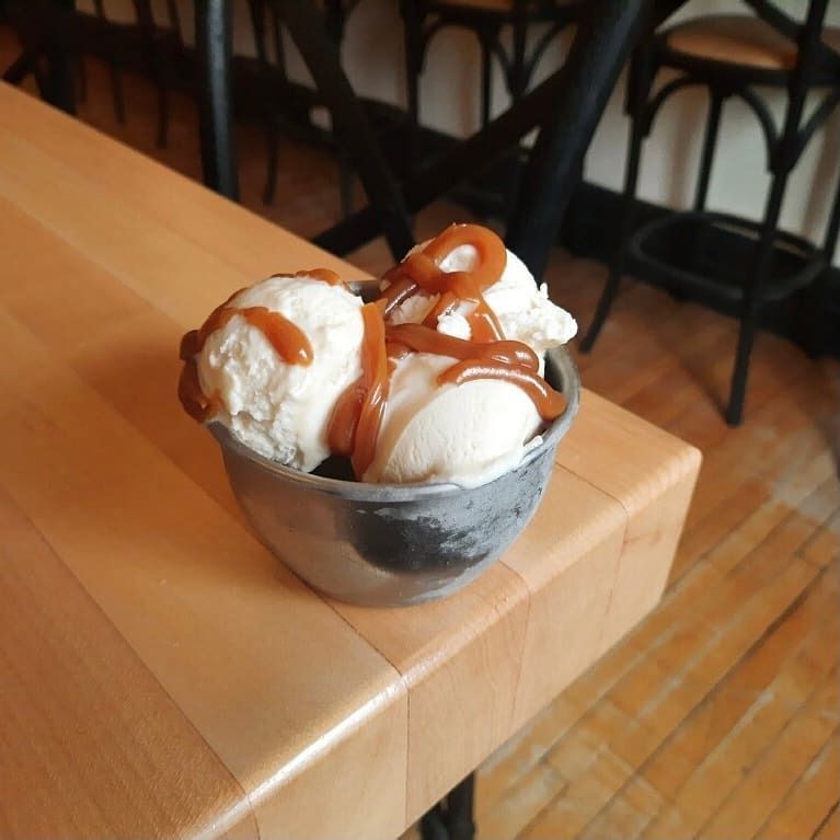 Bowl of vanilla ice cream drizzled with caramel on a wooden table in a café
