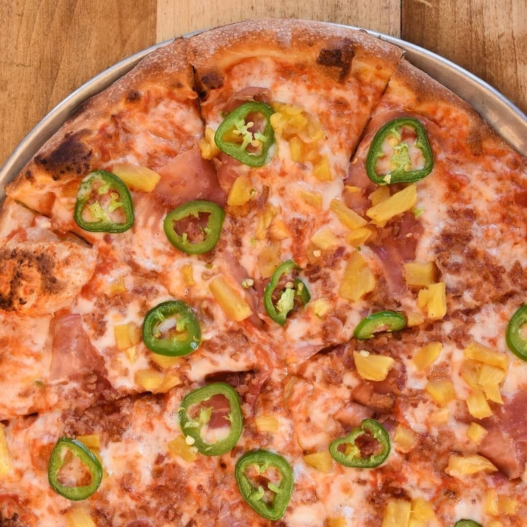 Close-up of a pizza topped with green jalapeño slices, pineapple, and melted cheese