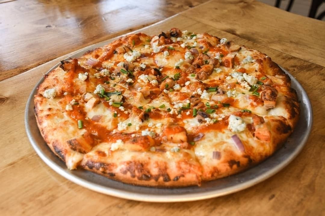 Cheesy pizza on a metal tray on a wooden table, topped with herbs and vegetables