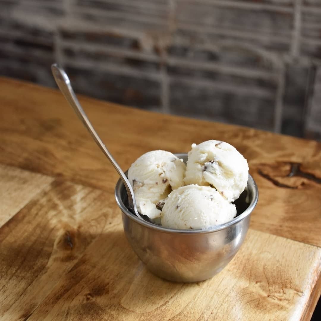 A metal cup of vanilla ice cream with chocolate chips and a spoon on a wooden table.