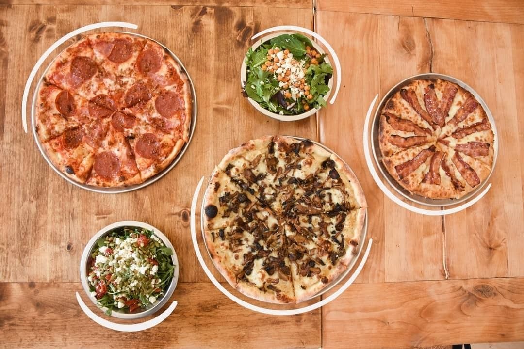 Five pizzas and two salads arranged on a wooden table from above