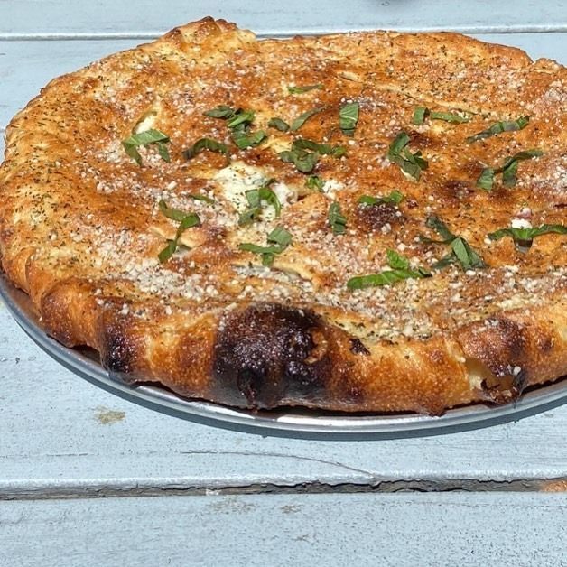 Round cheese pizza topped with basil on a metal tray