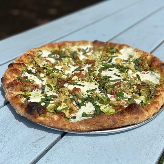 Pizza with melted cheese and herbs on a metal tray on a light blue table
