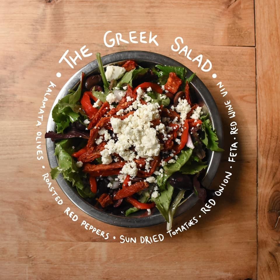 Greek salad in a bowl on a wooden table, topped with feta, olives, tomatoes, peppers, and lettuce.