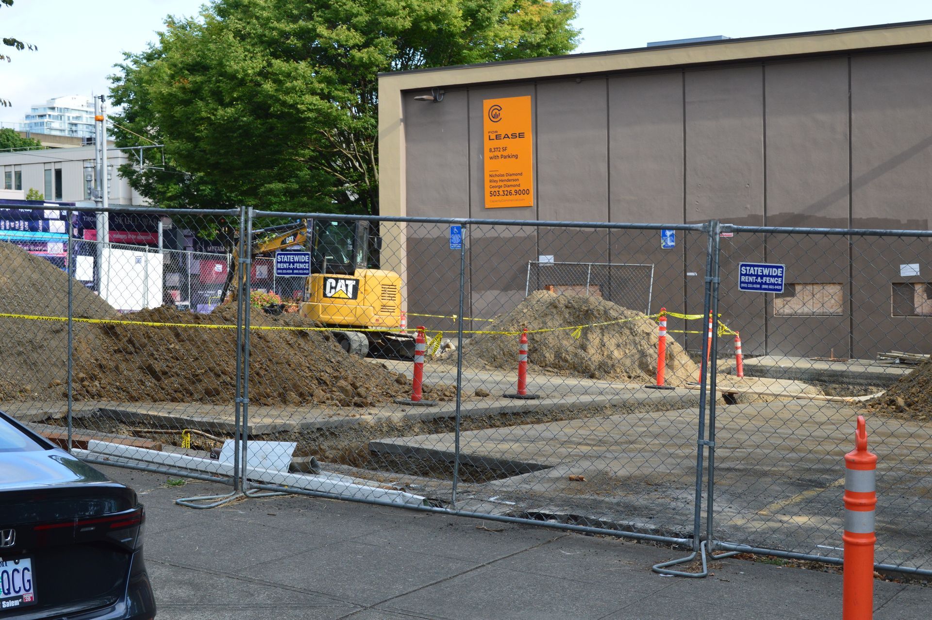 Construction site behind metal fencing with a yellow excavator and trees in the background