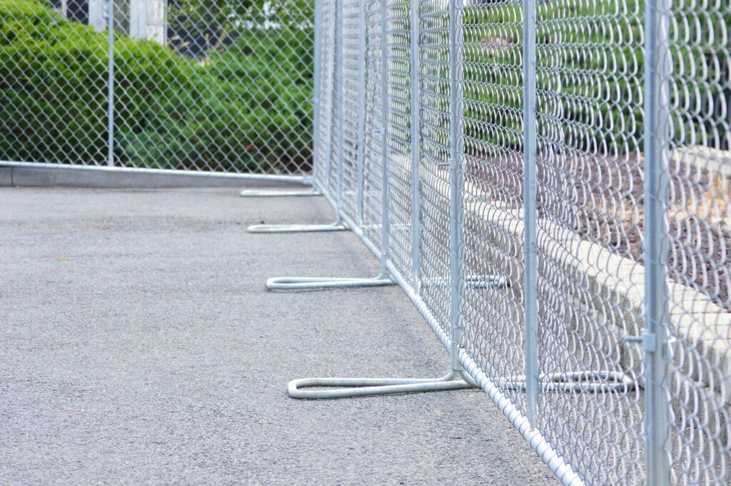 Temporary wire fence beside a paved walkway, enclosing a grassy area with covered objects under construction. Temporary wire fence beside a paved walkway, enclosing a grassy area with covered objects under construction.