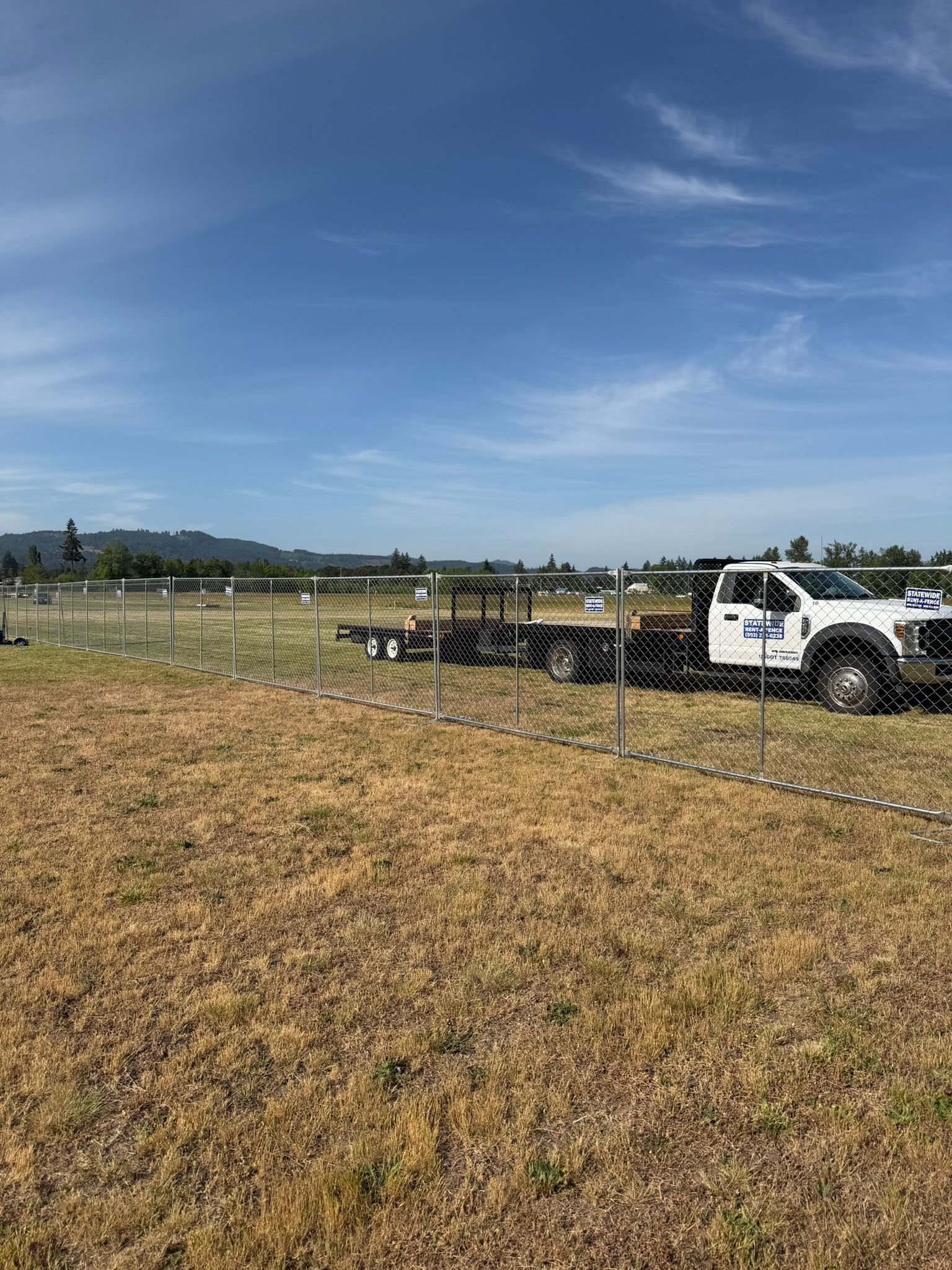 Stacks of black plastic crates and a wrapped pallet outdoors on grass under trees and blue sky