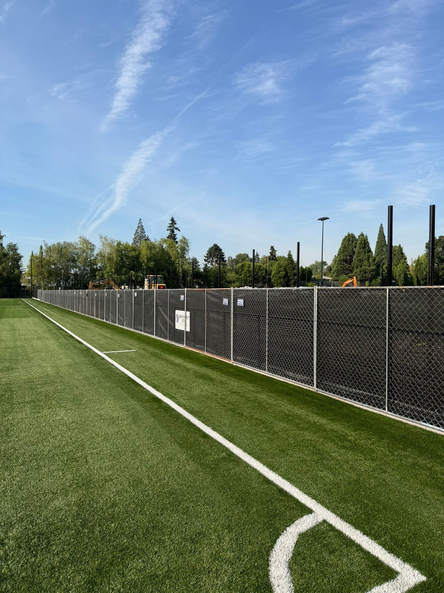 Empty soccer field corner with white lines, chain-link fence, and blue sky