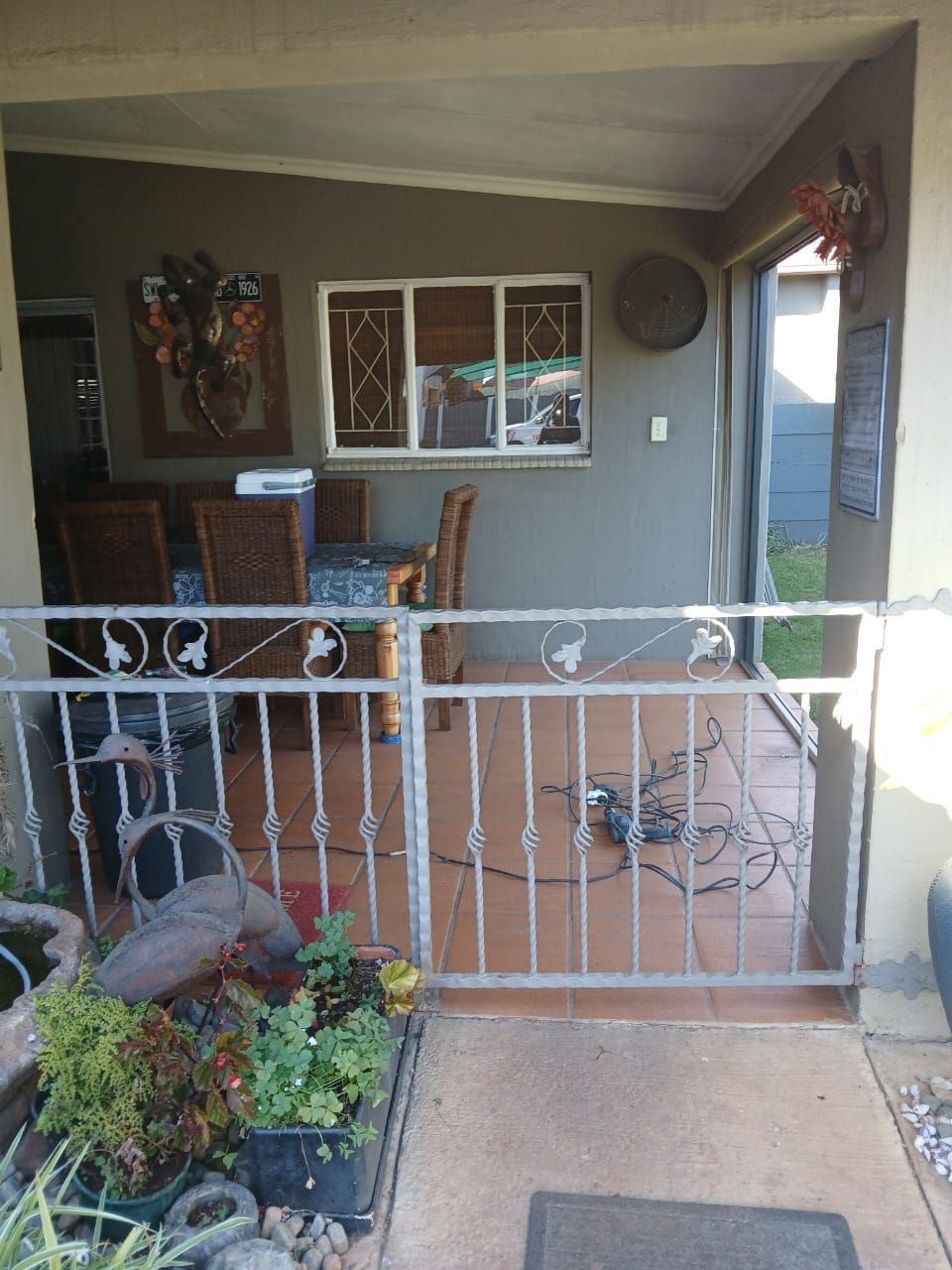 Front porch with white railing, table and chairs, potted plants, and an open front door
