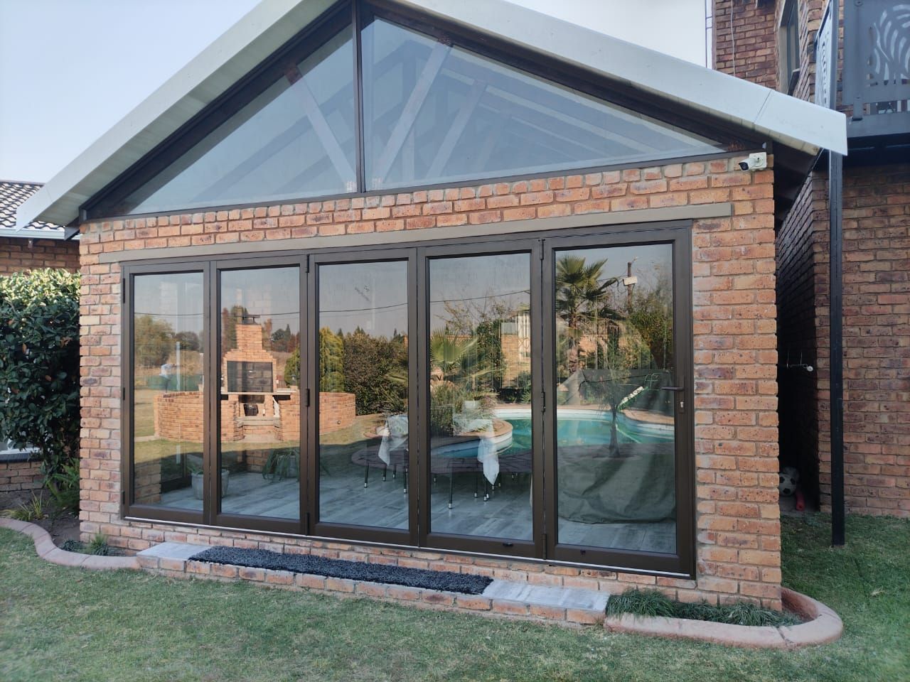 Brick garden room with large glass doors and triangular window roof under a sloped white frame