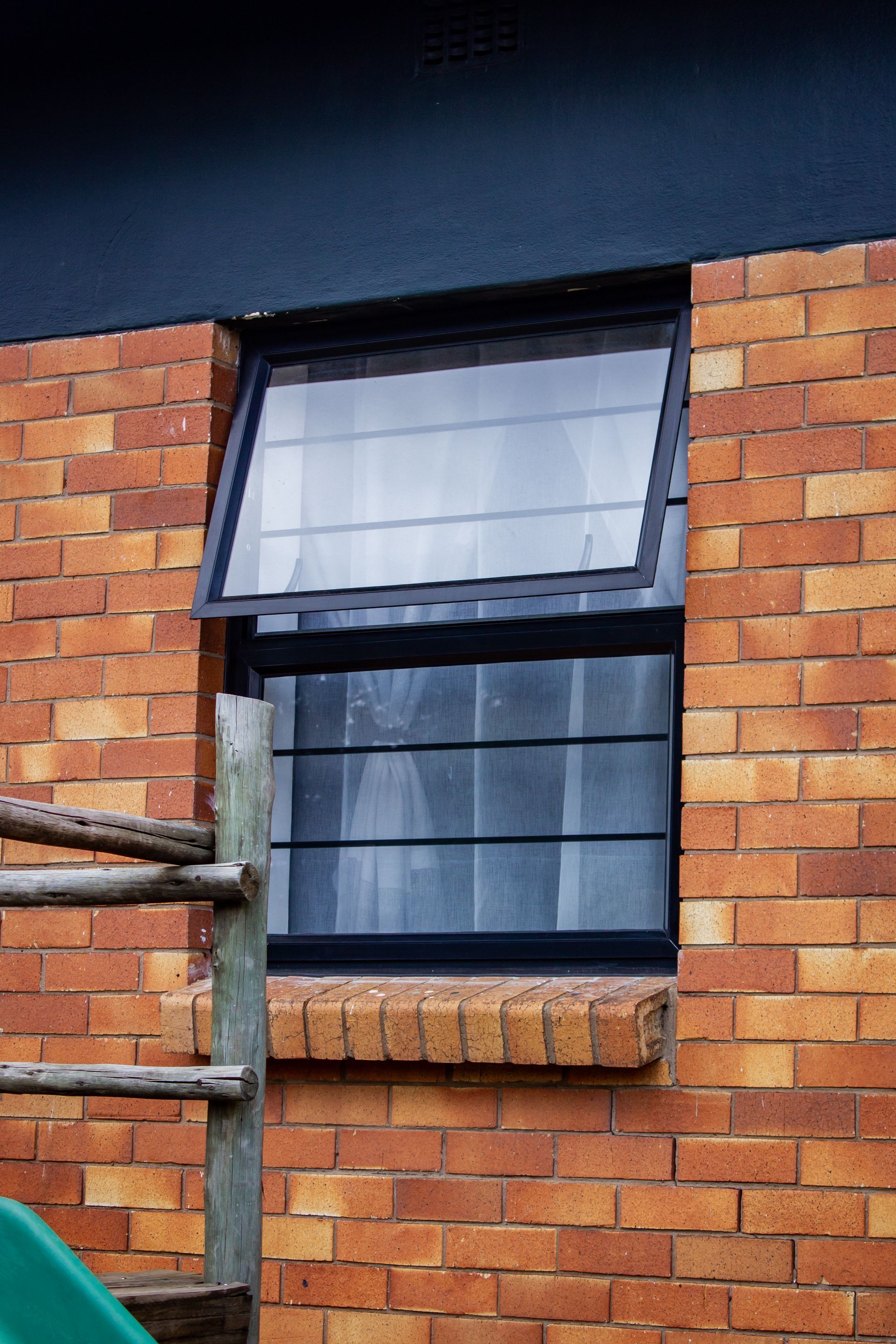 Open white-framed window on a red brick building with a dark awning above and pipes on the left