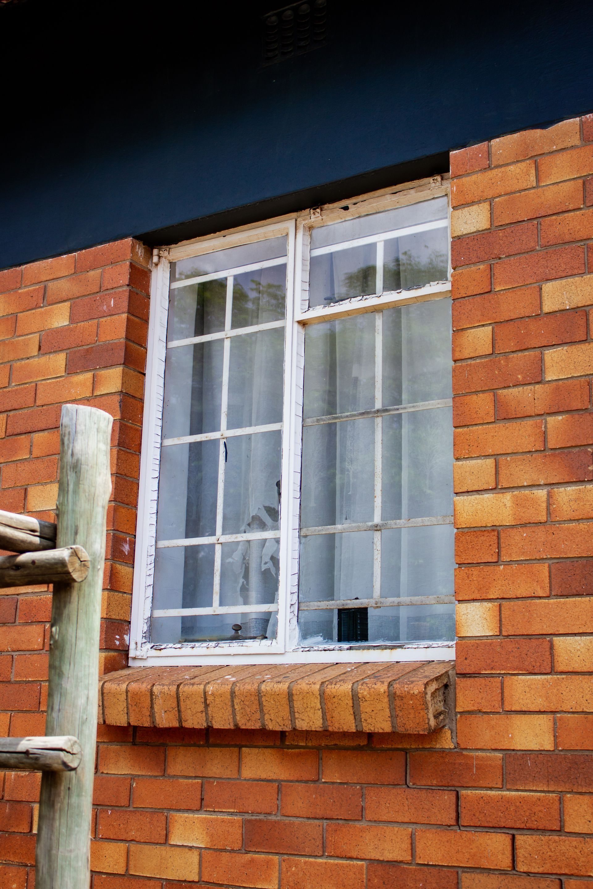 White-framed window in a red brick wall with a small brick sill and curtains behind the glass.