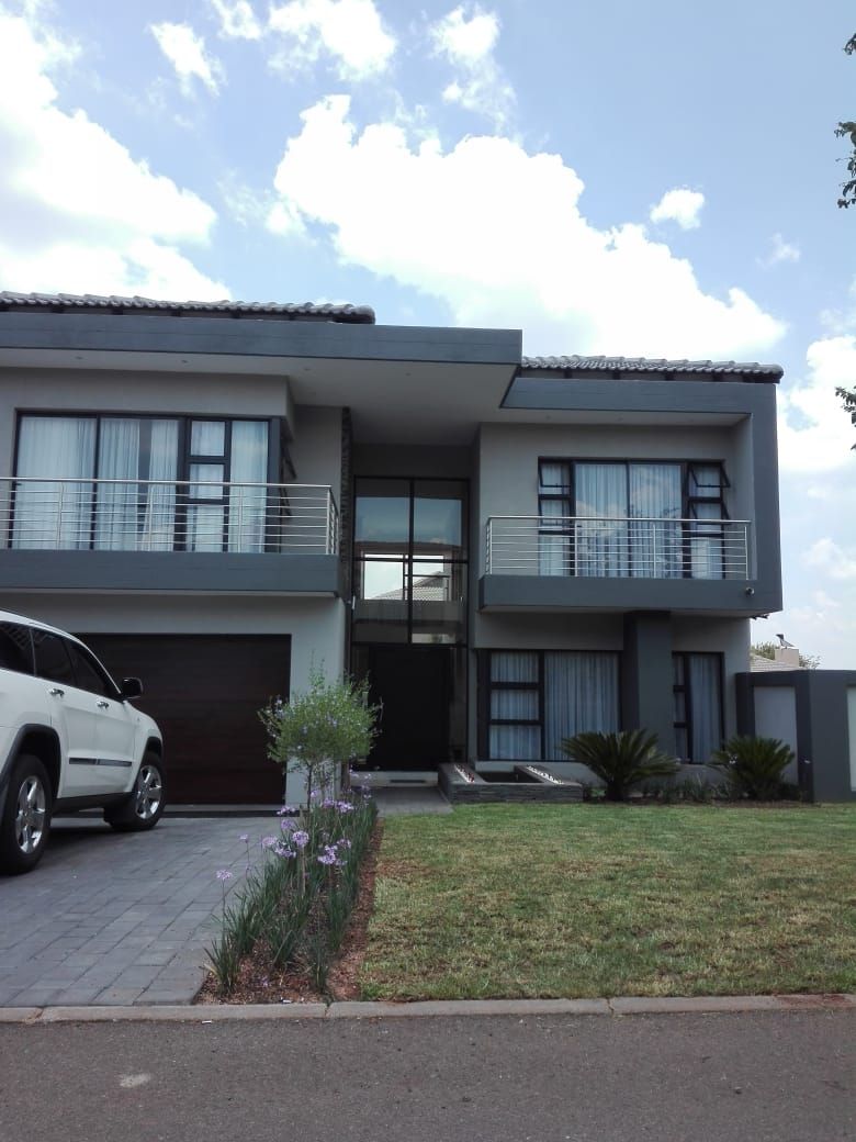 Modern two-story gray townhouse with balcony, driveway, white SUV, and front lawn under a cloudy sky