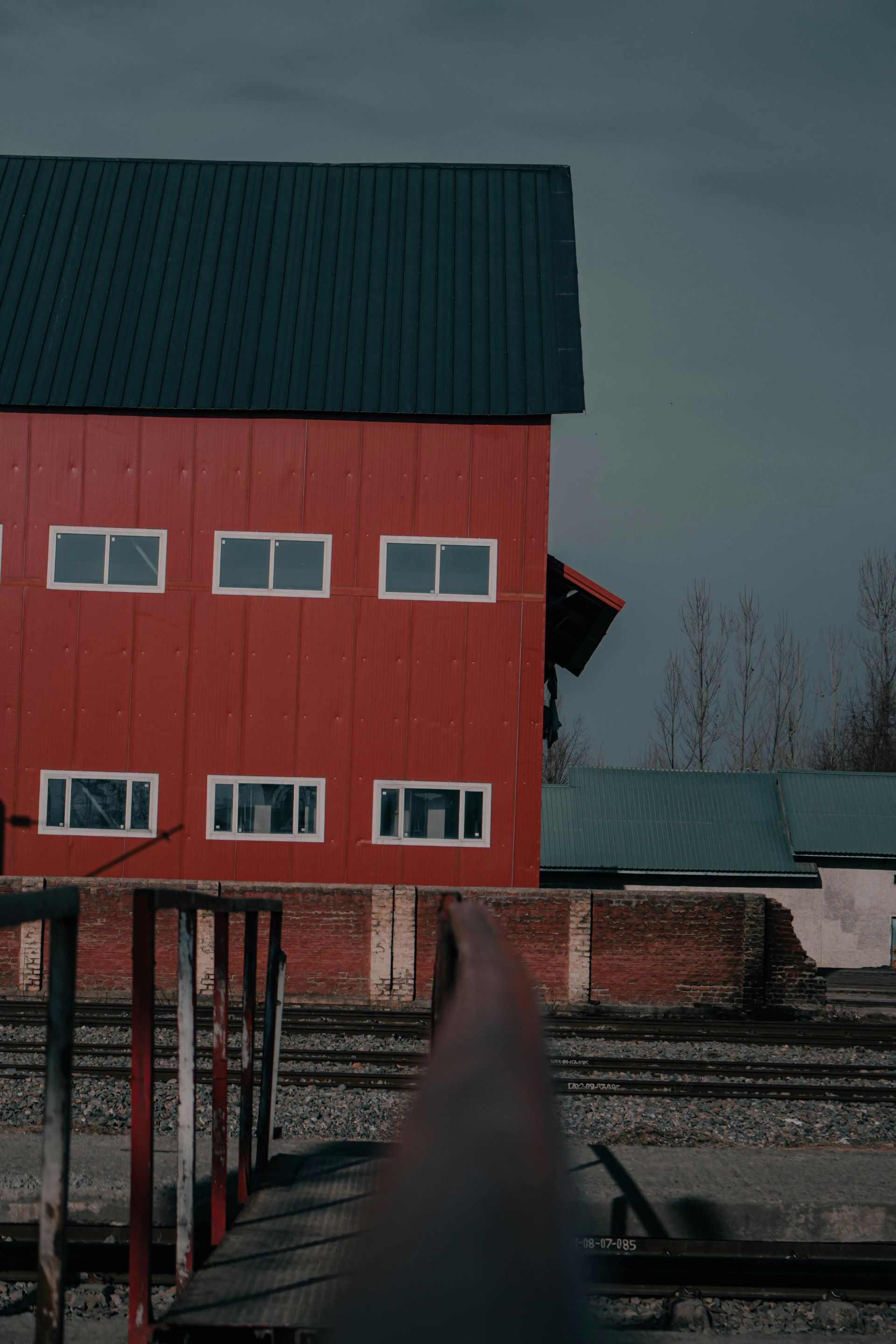 Red barn with teal roof beside a wooden dock under a gray sky.