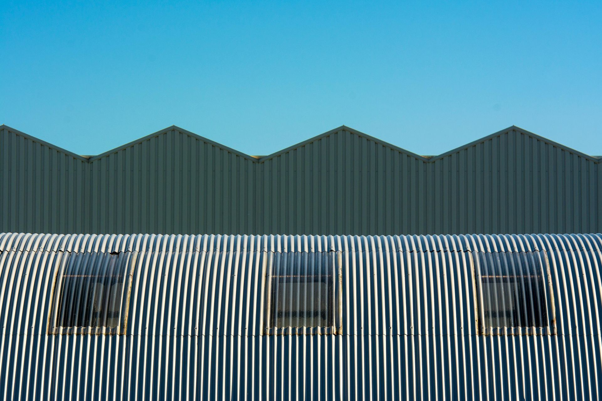 Blue corrugated metal building facade with three small windows under a teal zigzag roofline