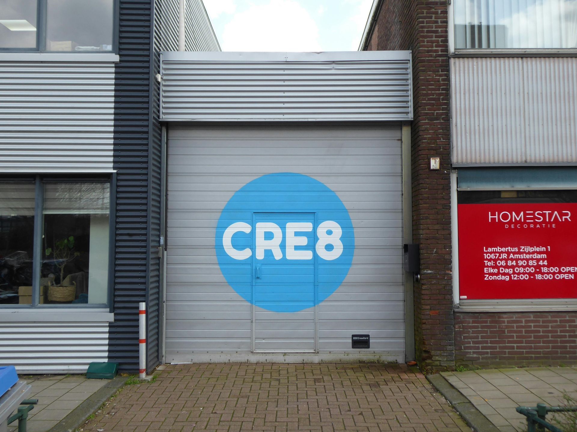 Storefront with a blue CRE8 sign on a gray roller door, next to a red HOMESTAR sign.