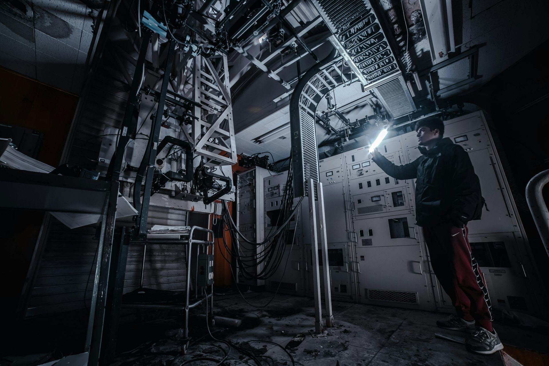 Top 3 Challenges in Multi-Family Electrical Work A person examines equipment in a dimly lit, industrial setting, holding a glowing light.