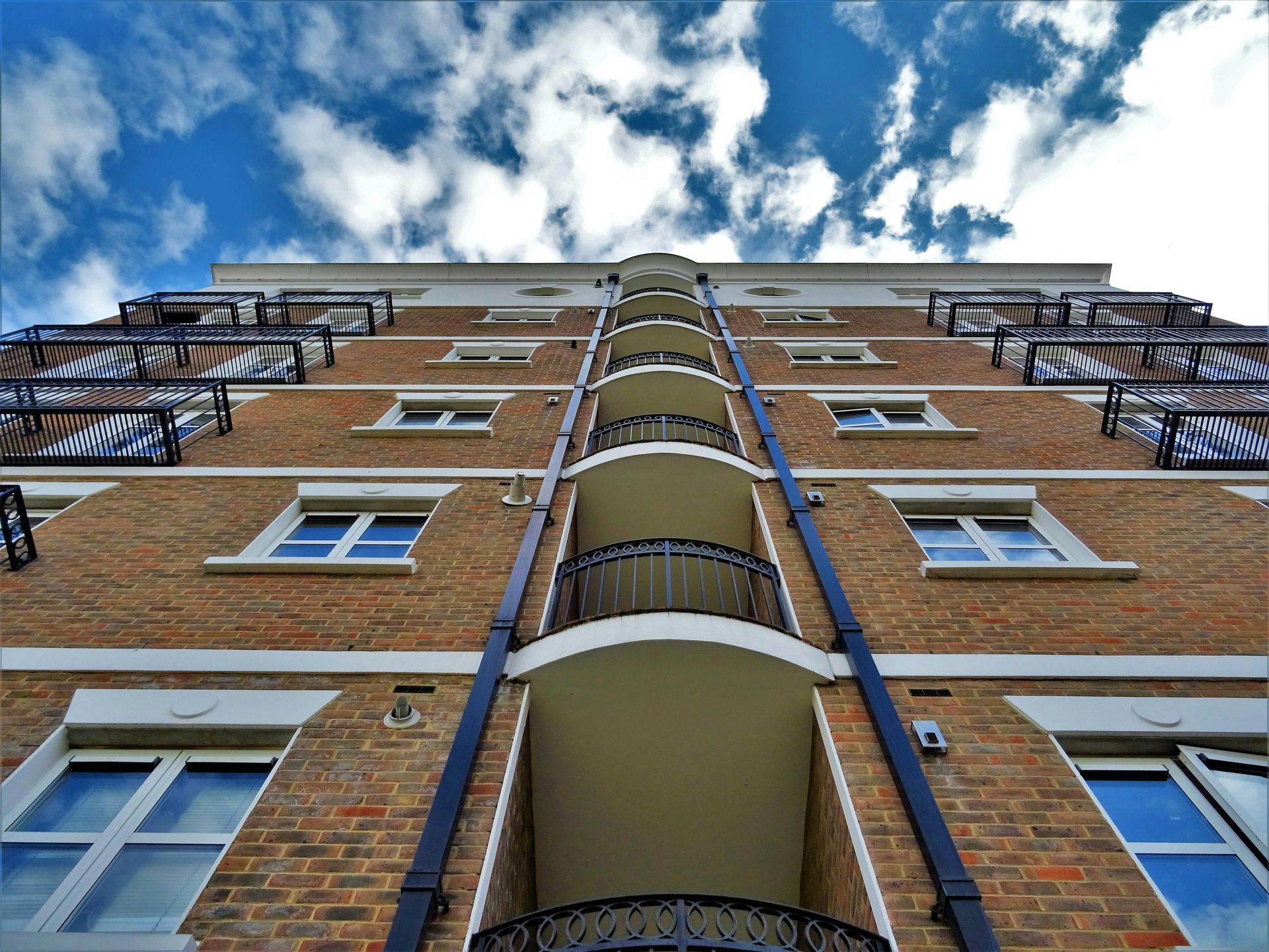 The Role of Electrical Contractors in Apartment Management Low-angle view of a brick apartment building with balconies against a blue sky with clouds.