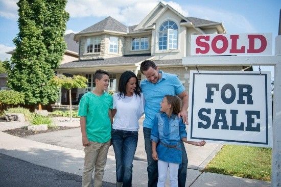 Family standing outside a house beside a sold for sale sign