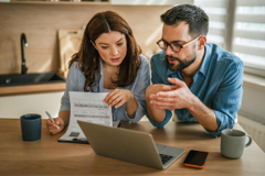 Two coworkers reviewing papers and a laptop at a wooden table in an office setting