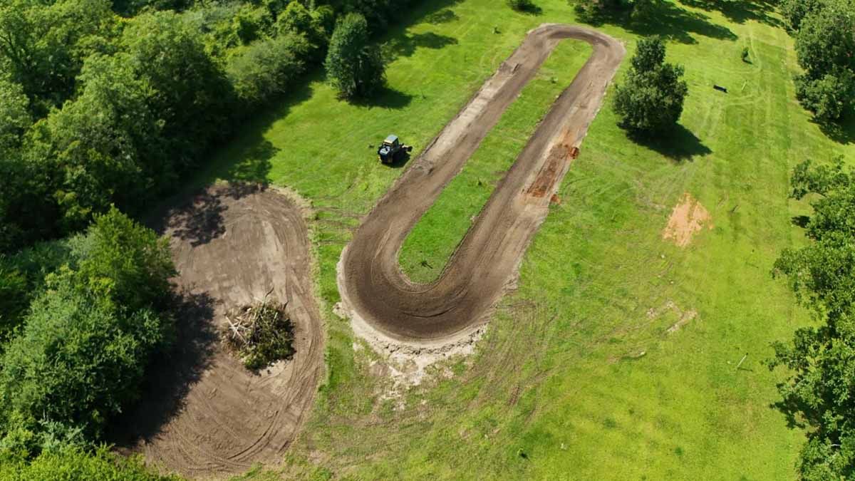 Aerial view of a dirt track and cleared land surrounded by trees and grass.