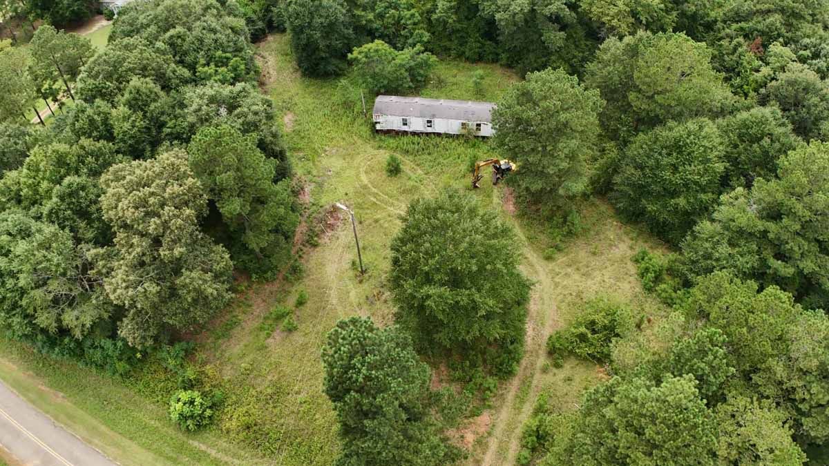 Aerial view of a small house surrounded by trees and a grassy clearing.