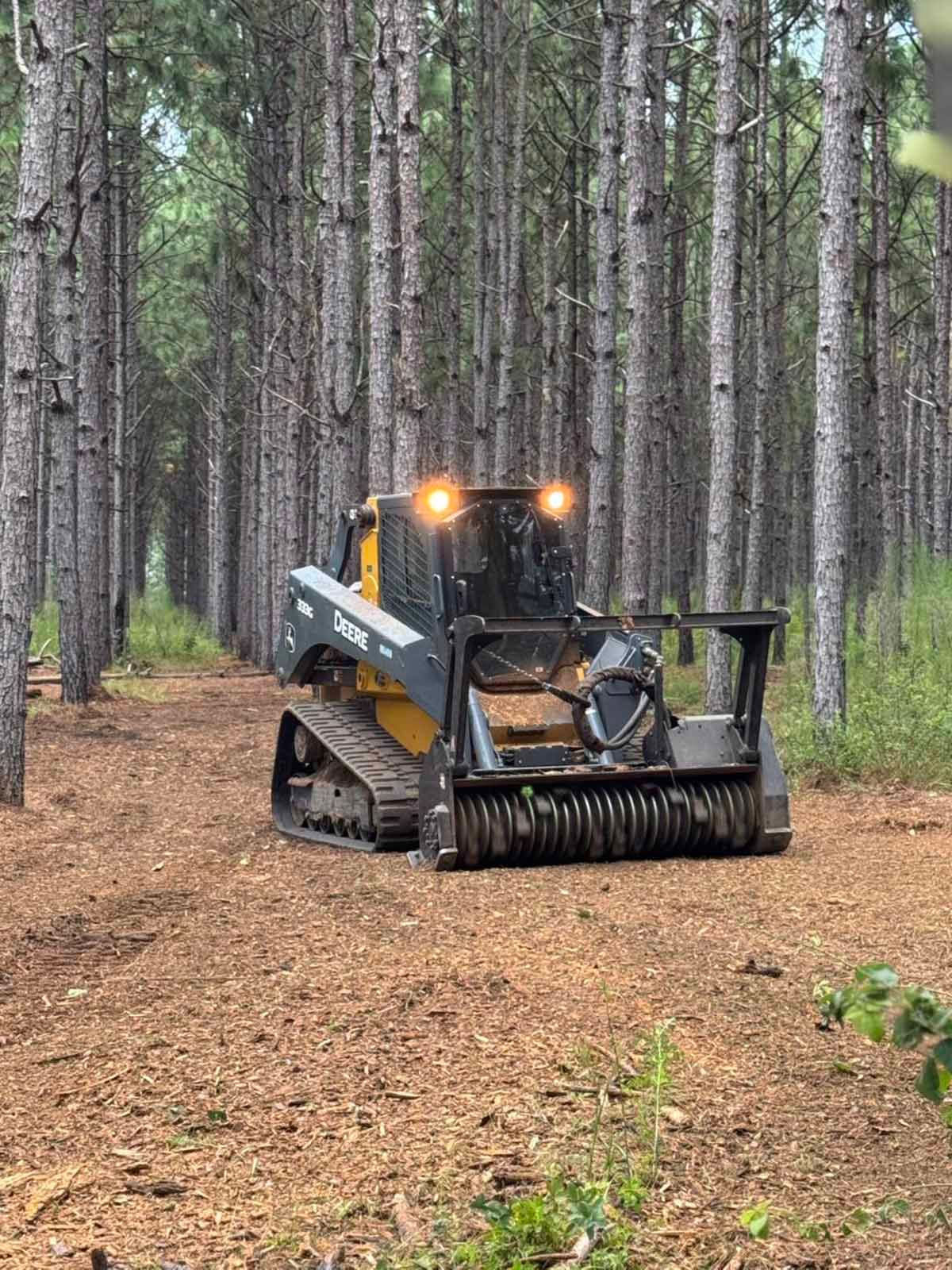 A tracked machine mulching a forest path, trees on both sides, in a wooded area.