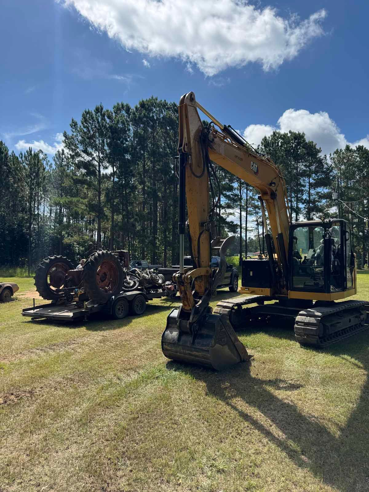Yellow excavator on grass next to a trailer carrying a red tractor on a sunny day.