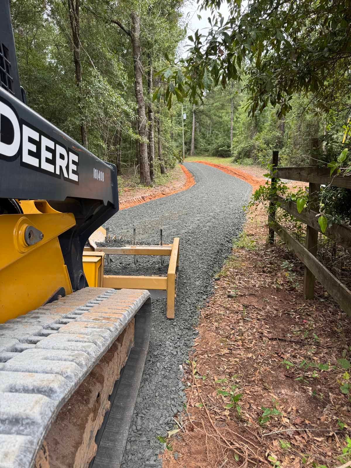 John Deere bulldozer grading a gravel path winding through a wooded area.