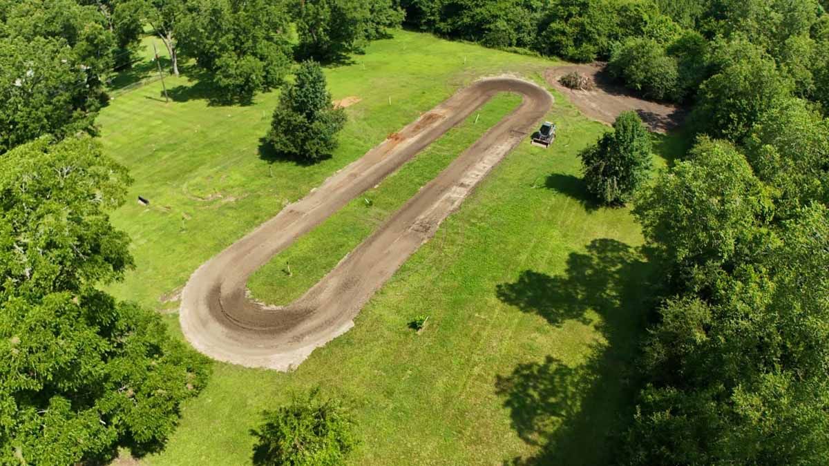 Aerial view of a dirt racetrack winding through a grassy field surrounded by trees.