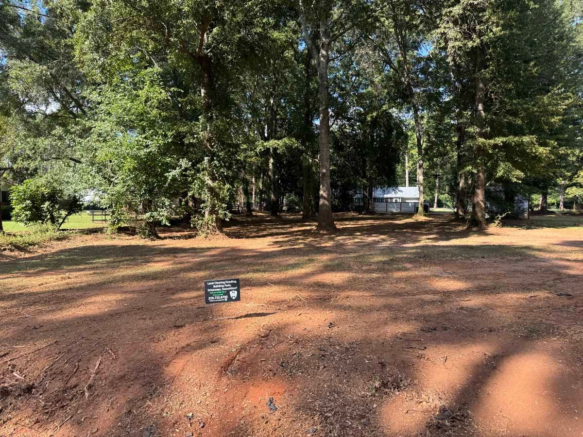 Open lot with dry, reddish soil, trees in the background, and a small sign in the foreground.