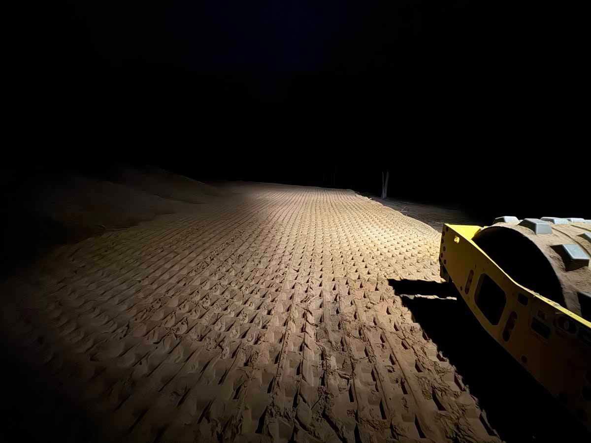 A yellow road roller illuminates a freshly graded road in the dark.