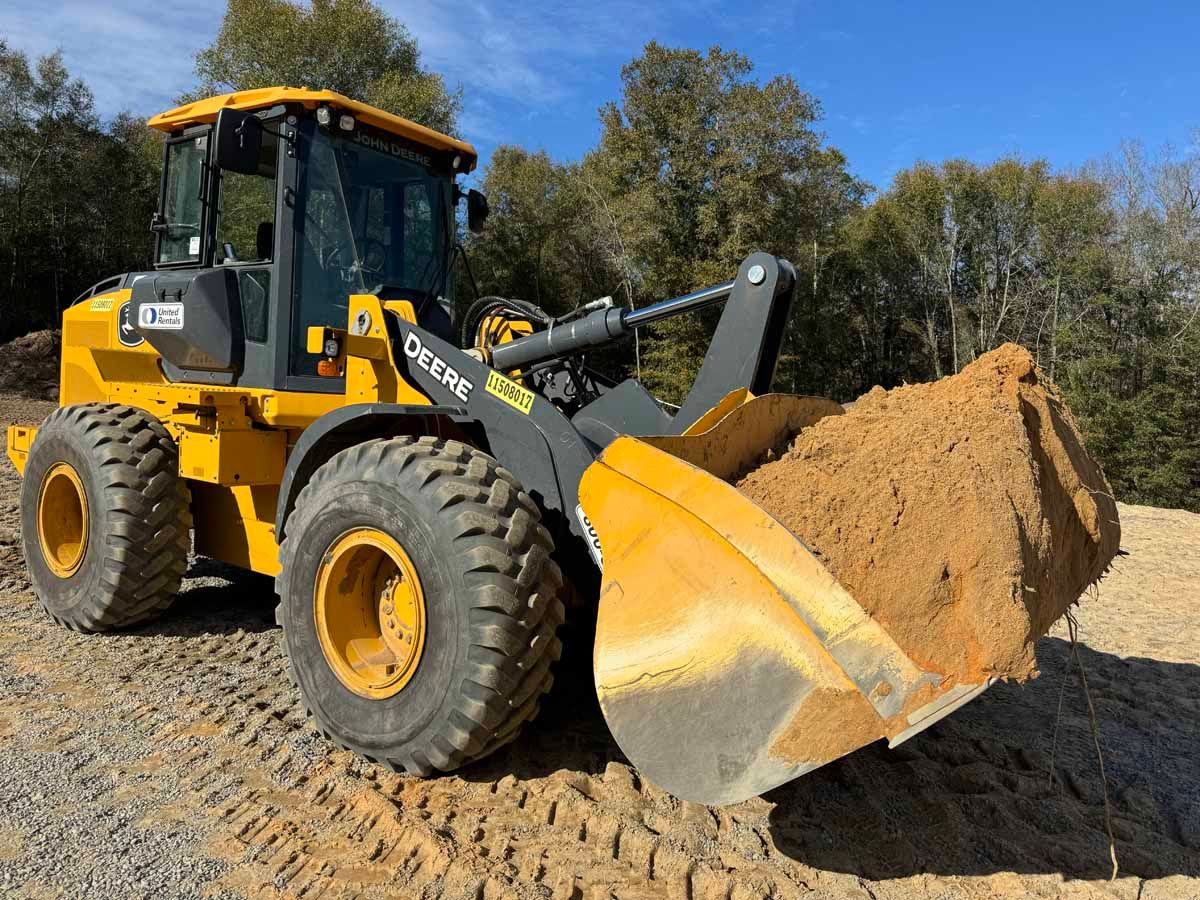 Yellow John Deere loader with a full scoop of tan material. Outdoors.