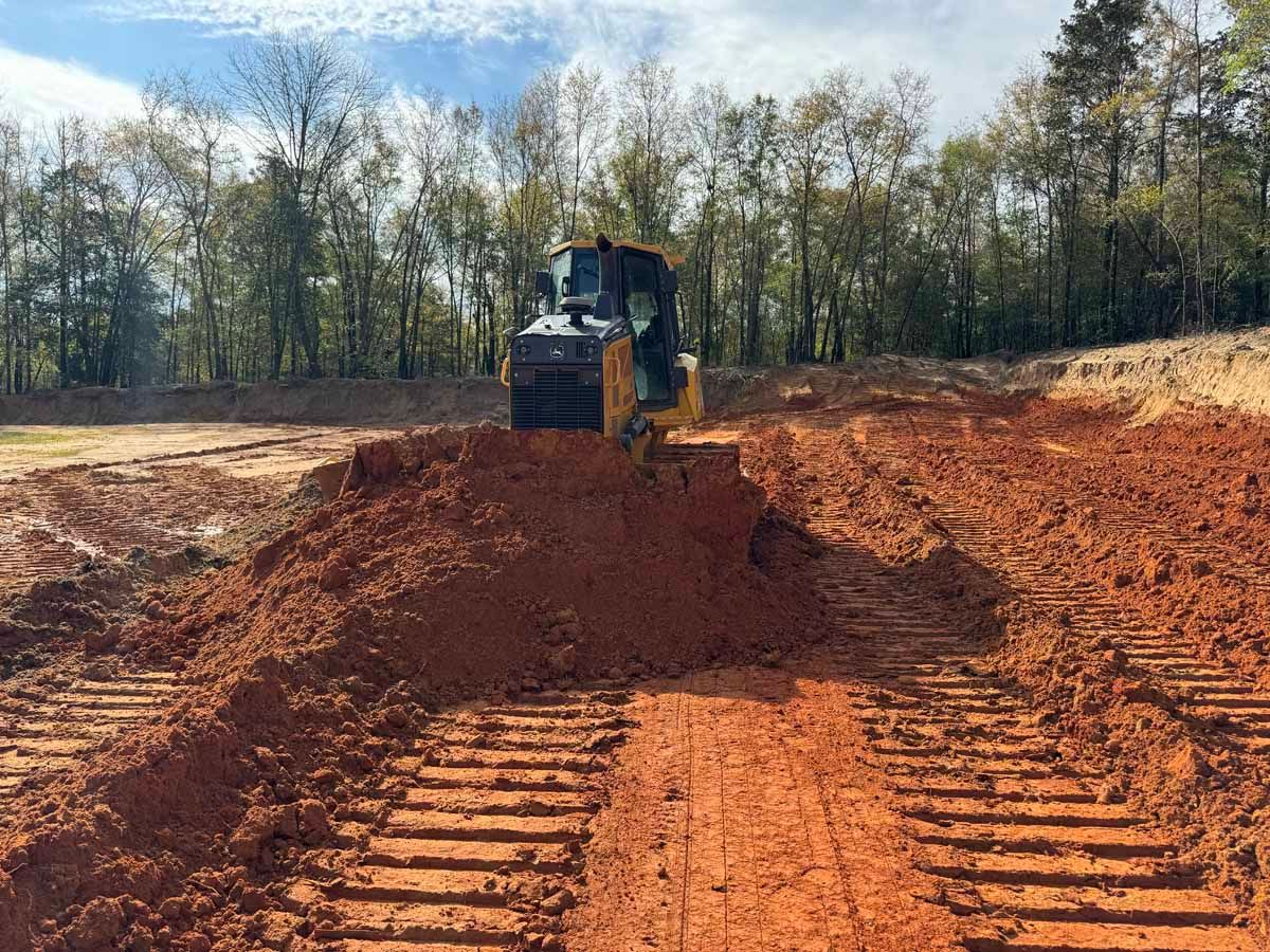 A bulldozer pushing reddish-brown soil on a construction site, tracks visible in the foreground.