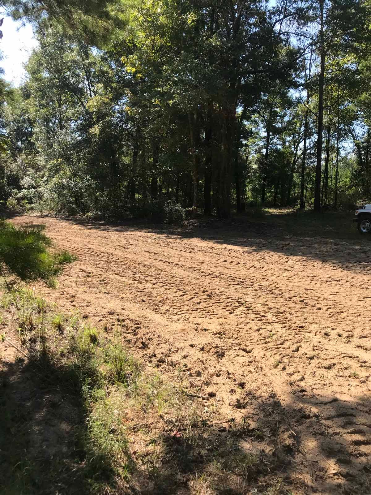 A cleared dirt area in a wooded setting, possibly for construction or a field.