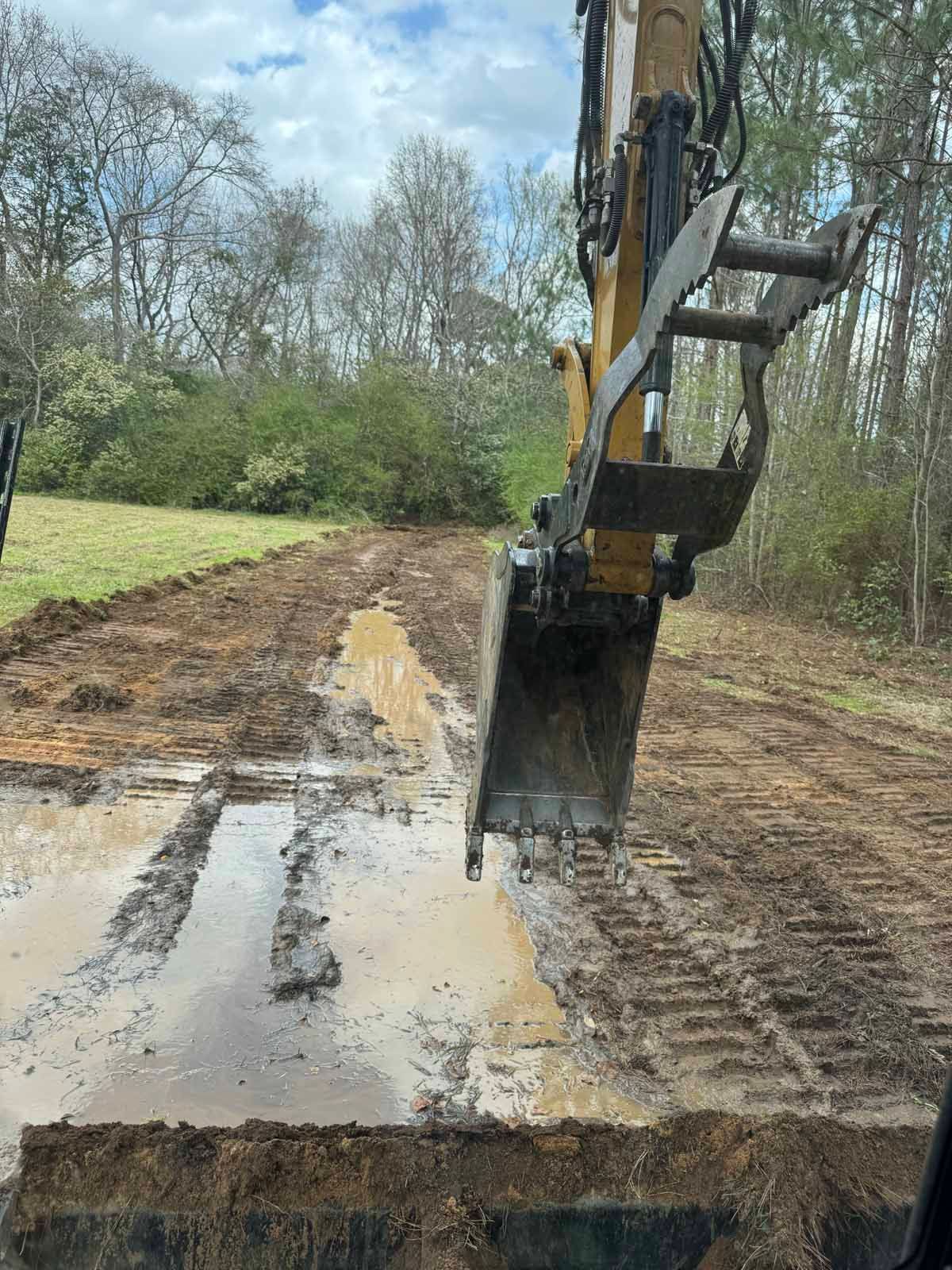 Excavator digging in muddy soil, creating a pathway in an outdoor setting.