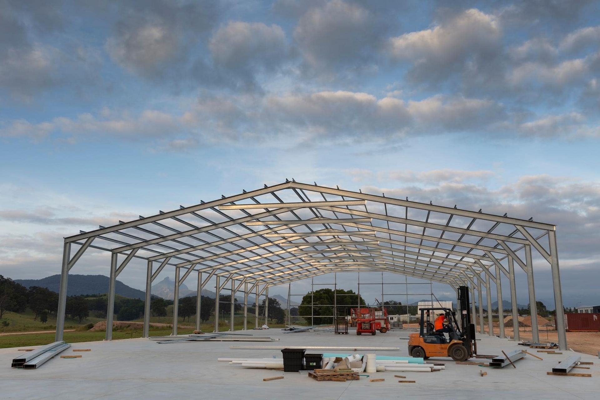 A Large Metal Structure is Being Built With a Forklift in the Foreground — Mbah Metal Roofing in South Mullumbimby, NSW