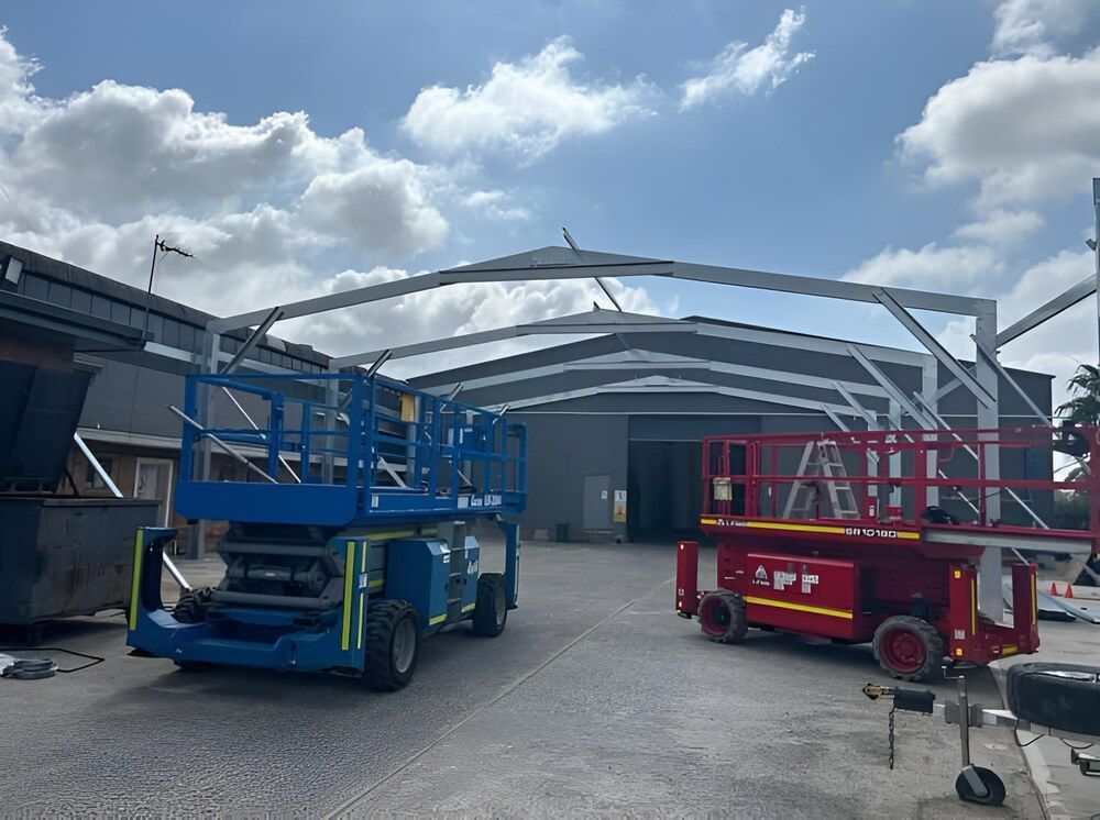 Two Scissor Lifts Are Parked In Front Of A Building — Mbah Metal Roofing In Murwillumbah, NSW