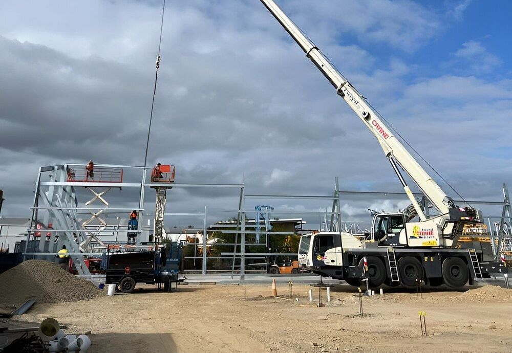 A Large Crane Is Lifting A Piece Of Metal In A Construction Site — Mbah Metal Roofing In Murwillumbah, NSW