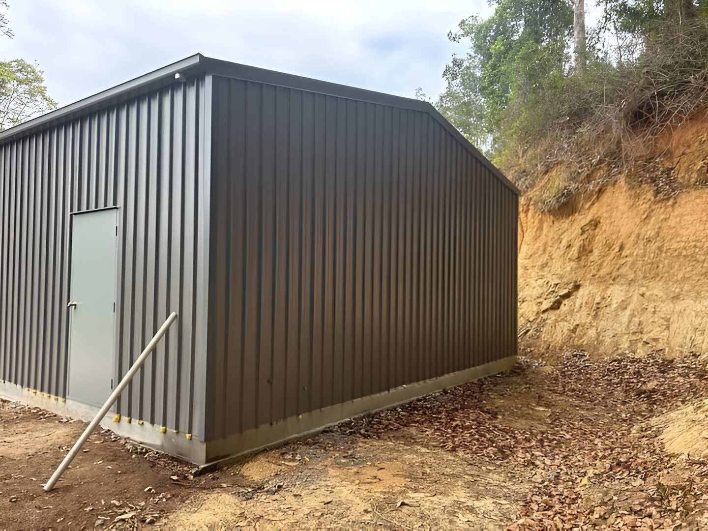 A Large Metal Building Is Sitting On Top Of A Dirt Hill — Mbah Metal Roofing In Murwillumbah, NSW