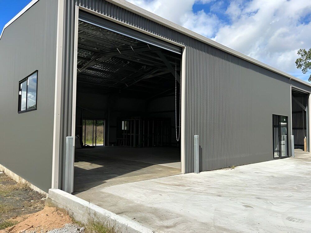 A Large Gray Building With A Sliding Door Is Being Built — Mbah Metal Roofing In Murwillumbah, NSW