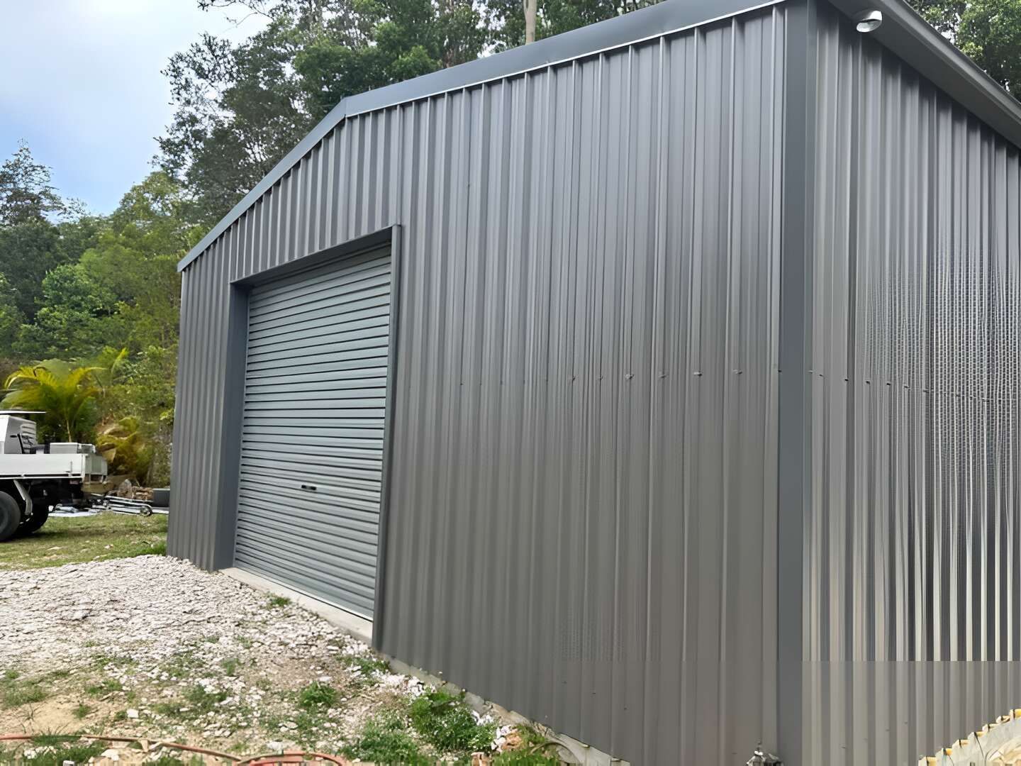 A Gray Metal Building With A Truck Parked In Front Of It — Mbah Metal Roofing In Murwillumbah, NSW