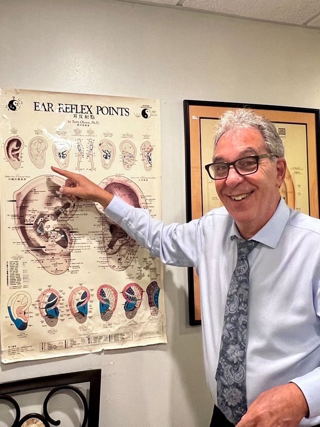 A smiling man in a dress shirt and tie points at an educational chart titled