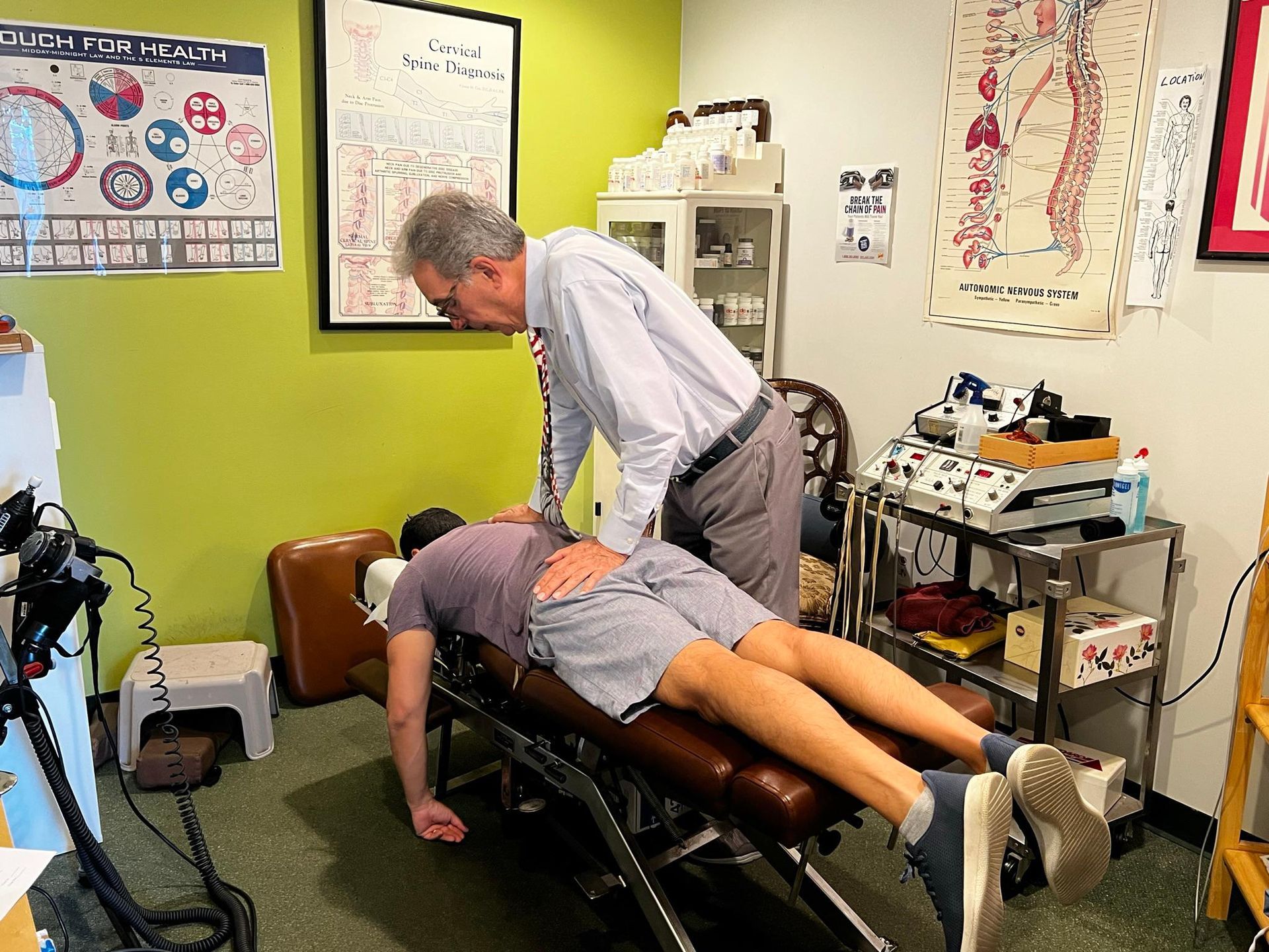 A chiropractor adjusts a patient lying facedown on a treatment table in a clinical office.