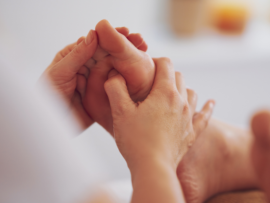 Hands performing a professional foot massage, focusing on the sole in a soft, bright, clinic setting.